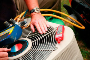 HVAC technician inspecting air conditioning unit with diagnostic tools and yellow service hoses visible.