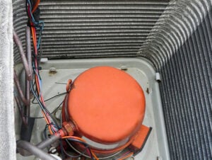 Orange AC compressor with red wiring inside HVAC unit showing internal cooling system components and fins.