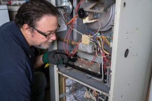 Technician in safety glasses inspecting internal furnace components with wiring and heating elements visible.