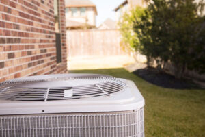 Outdoor air conditioning unit installed next to brick house with yard and landscaping in background.