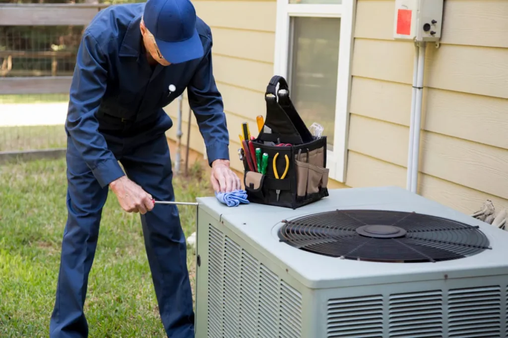 Professional HVAC technician in blue uniform cleaning air conditioning unit outdoor condenser with tools and equipment nearby.