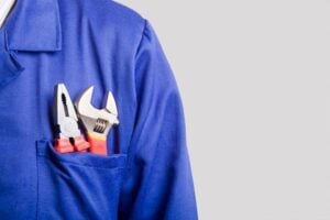 Plumber or HVAC technician wearing blue work uniform with adjustable wrench and pipe wrench tools in chest pocket.