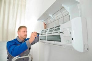 Professional technician in blue uniform servicing and installing a white wall-mounted air conditioning unit indoors.