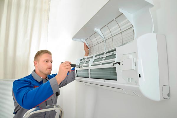 Professional technician in blue uniform servicing and installing a white wall-mounted air conditioning unit indoors.