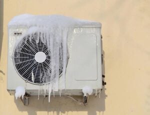 Outdoor AC condenser unit covered in thick ice accumulation on fan and housing components.