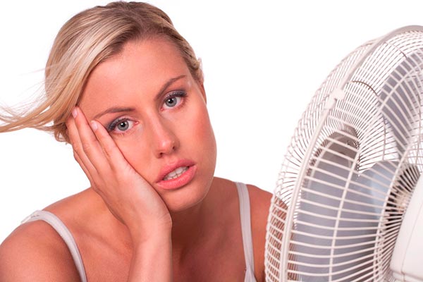 Woman looking uncomfortable while sitting near a fan, illustrating common air conditioning problems and the need for HVAC repair.