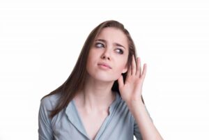 Woman with hand to ear listening intently, concerned expression on face while detecting hissing sound from heater system.